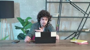 Genç kıvırcık saçlı adam internette konuşmak için dizüstü bilgisayar kullanıyor..