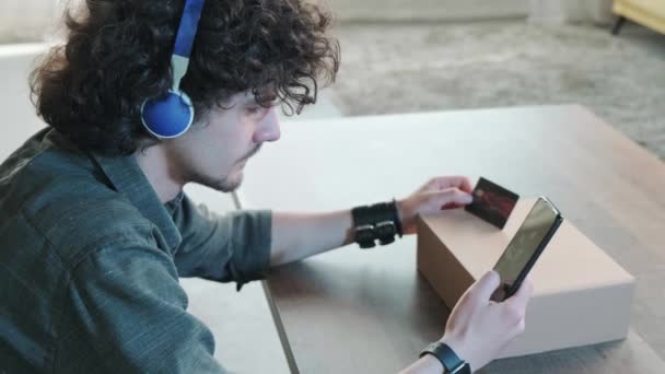 Boční pohled na muže nakupování online s kreditní kartou pomocí chytrého telefonu doma. — Stock video