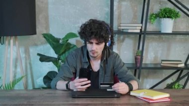 Genç adam evde akıllı telefon kullanarak internet üzerinden alışveriş yapıyor..