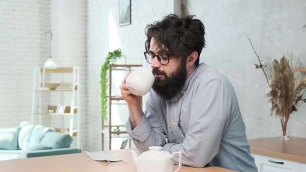 Bel homme barbu dans la cuisine profiter d'une tasse de thé après une dure journée de travail — Video