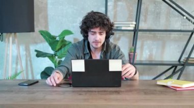 Genç kıvırcık saçlı adam internette konuşmak için dizüstü bilgisayar kullanıyor..