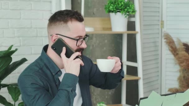 Szakállas férfi kávét iszik, miközben telefonál a barátjával.. — Stock videók