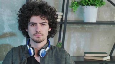 Yakışıklı, kıvırcık saçlı, mutlu bir yüz ifadesiyle kameraya bakan adam..