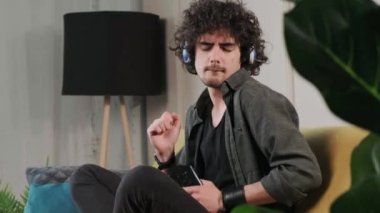 Kanepede kıvırcık saçlı genç adam kulaklıkla müzik dinliyor..