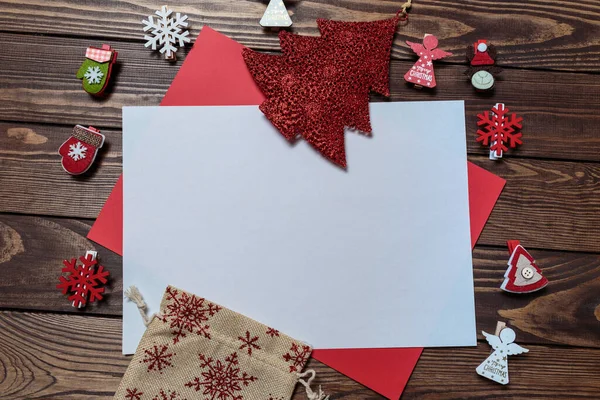 Yılbaşı kartı. Noel oyuncakları ve sembollerle süslenmiş tahta bir masanın üzerinde beyaz boş bir çarşaf. Melekler, kar taneleri, hediye paketi. Noel Baba 'ya mektup.