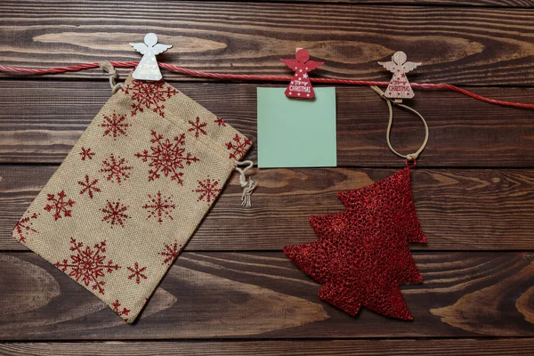 christmas card. christmas mockup. a blank sheet, a gift bag and a Christmas tree hang on a red rope. wooden background. a Christmas tree and a bag for gifts lie on a wooden table. mockup.