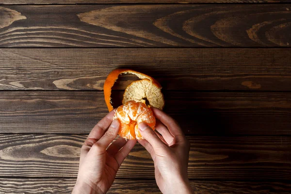 girl cleans a tangerine. view from above. hands clean the tangerine. wooden table.