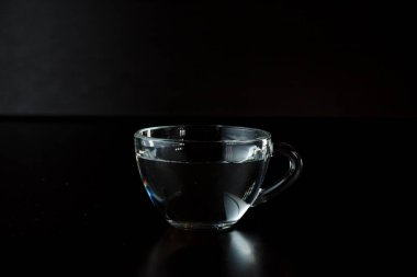 Koyu arkaplanı su olan şeffaf cam bardak. Masanın üzerinde bir fincanda iç. Alkol. susuzluğu gidermek.