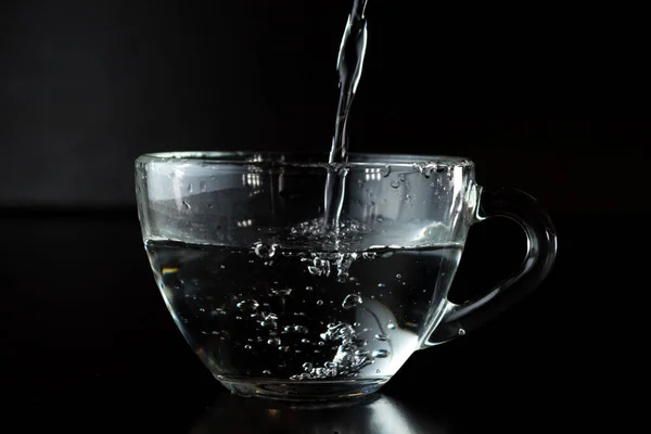 コップに水を注ぐのです 暗い背景に水を入れた透明なカップ ウォータージェット 有機水だ きれいな水の概念 サイドビュー — ストック写真