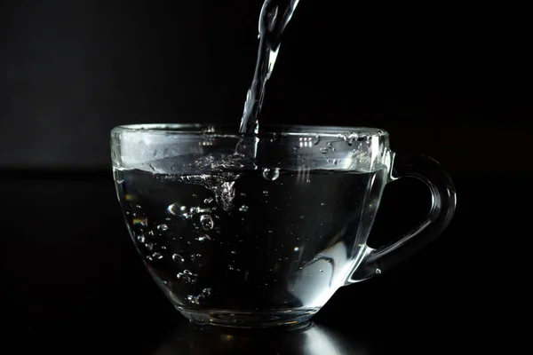 コップに水を注ぐのです 暗い背景に水を入れた透明なカップ ウォータージェット 有機水だ きれいな水の概念 サイドビュー — ストック写真