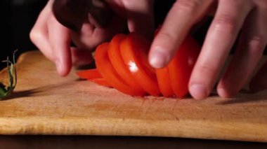 Adam olgun kırmızı bir domatesi bıçakla kesiyor. Kesme tahtasında domates.