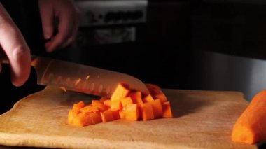 Havuç dilimliyorum. Adam havuçları bıçakla küp küp doğradı. Kesme tahtasındaki sebzeler. Evde pişir..