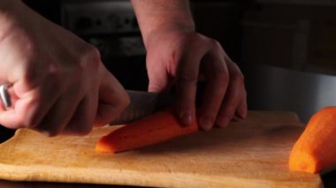 Havuç dilimliyorum. Adam kesme tahtasındaki havuçları dilimlere ayırıyor. Evde pişir..