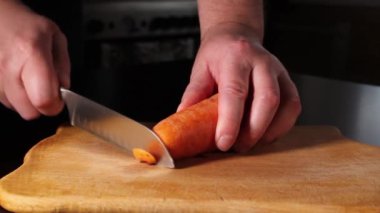İnsanlar havuç soyarlar. Kesme tahtasındaki sebzeler. Şef, havucun kenarlarını bıçakla kesiyor. Evde pişir..