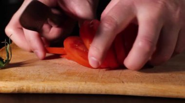 Adam olgun kırmızı bir domatesi bıçakla kesiyor..