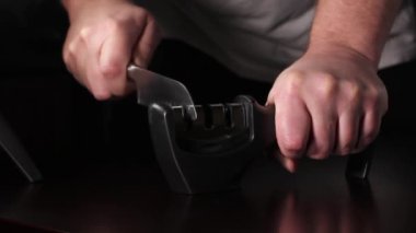 Bir adam bileyiciyle bıçağı keskinleştirir. Karanlık bir arka planda eylem. & Kapat.