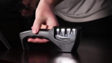 Bir adam bileyiciyle bıçağı keskinleştirir. Karanlık bir arka planda eylem. & Kapat.