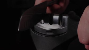 Bir adam bileyiciyle bıçağı keskinleştirir. Karanlık bir arka planda eylem. & Kapat.