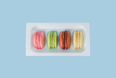 Bir kutuda çok renkli badem kurabiyesi seti. Makarnalar mavi üzerine izole edilmiş. Tatlılar moda oldu. Yukarıdan bak. Boşluğu kopyala.