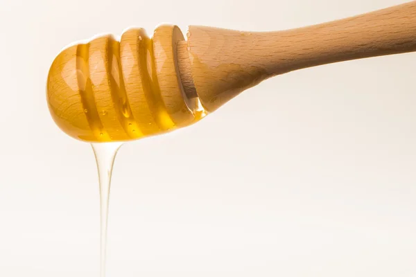 Honey dripping from a wooden honey dipper isolated on white back — Stock Photo, Image