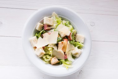 Tavuklu Sezar salatası ve ahşap masada yeşiller.