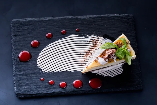 Beyaz ahşap masa üzerinde çilek şurubu ile lezzetli peynirli kek