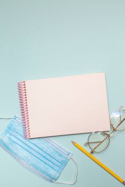Gözlük, boş defter, yeşil arka planda yazıtlar, tıbbi maske ve kalem için yer var.