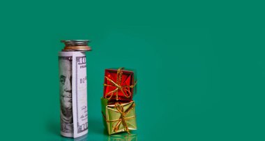 Bozuk paralarla dolu bir tomar para ve yeşil arka planda küçük hediye kutuları. Yeni yıl konsepti
