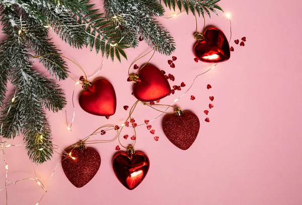 Árbol de Navidad con juguetes rojos, corazones y una guirnalda luminosa sobre un fondo rosa — Foto de Stock