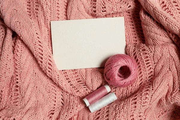 Wit vel voor het invoegen van tekst met een bol wol en draden op een roze gebreide stof — Stockfoto