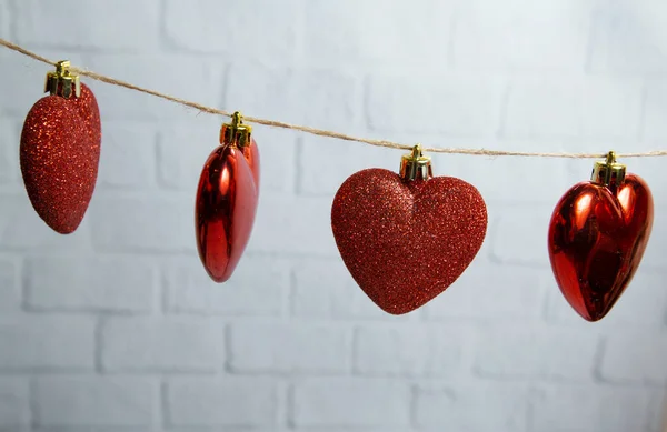 Red hearts hang on a thread on a white brick background — Stock Photo, Image