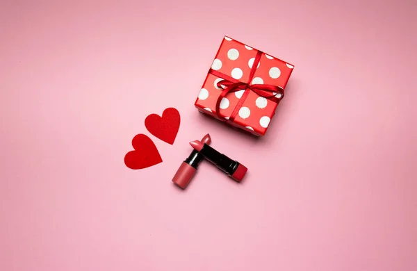 선물 상자에 립스틱을 꽂고 핑크 색 배경에 작은 하트를 꽂는다 — 스톡 사진