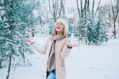 Genç kız gülüyor ve karlı bir parkta kar atıyor. Ön planda kar taneleri