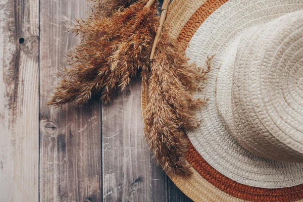 straw brown and beige hat and dry branches of reeds on a wooden background. summer hat with brim . High quality photo