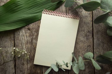 Ahşap arkaplanda bitki yaprakları ve okaliptüs filizi olan boş spiral defter. Yukarıdan bak. düz yat