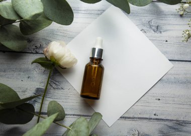 Hyaluronik serum ve kozmetik şişelerle dolu cam bir şişe okaliptüs dalları ve bitkilerle çevrili hafif ahşap bir zemin üzerinde yatar. kozmetik ürünü