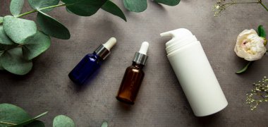 Okaliptüs filizi ve yeşil yapraklı gri arka planda serum ve kozmetik krem dolu şişeler. seçici odak