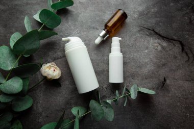 Okaliptüs filizi ve yeşil yapraklı gri arka planda serum ve kozmetik krem dolu şişeler. seçici odak