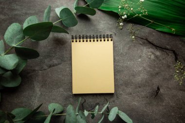 Üzerinde bitki yaprakları ve okaliptüs filizi olan gri arkaplandaki yazı için yeri olan boş spiral bir defter. Yukarıdan bak. düz yat