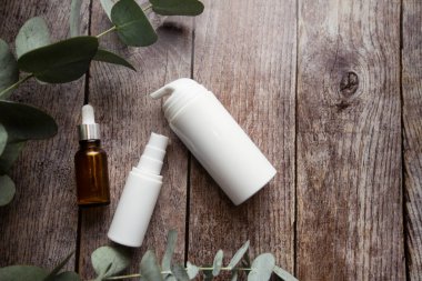 Plastik ambalajlar ve yapraklı doğal organik kozmetik ürünleri içeren şişeler. Şişe markalaşmak için hazırlandı. Ahşap arka planda kozmetik ürünleri