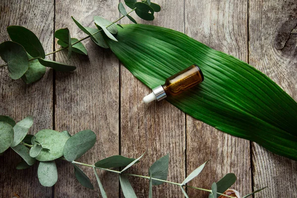 Glass dropper bottle with pipette. bottle with transparent hyaluronic cosmetic serum and skin care concept on wooden background with green leaves and eucalyptus sprig