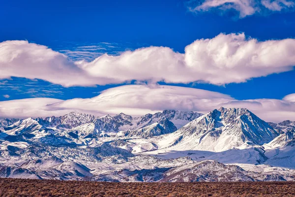 カリフォルニア州の東シエラネバダ山脈の雪の山の峰の上に白い雲と強烈な青い空米国 — ストック写真
