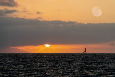 Orange Cloudy Sky 'da güneş batarken Okyanus boyunca bir tekne yüzüyor.