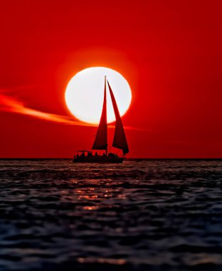 Bir yelkenli okyanus boyunca yol alıyor Arkaplanda canlı renkli bir günbatımı var