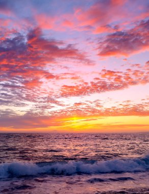 A Colorful Ocean Sunset Sky as a Gentle Wave Rolls to Shore in a Vertical Image Format clipart