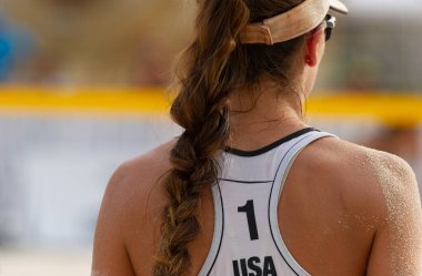 Dişi bir plaj voleybolcusu topu servis etmeye hazırlanıyor.