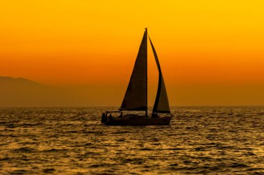 Okyanusta rengarenk bir gün batımıyla bir yelkenli yelkenli yelken açıyor.