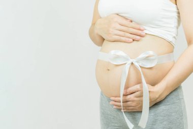 Karnında beyaz kurdele olan hamile bir kadının karnının seçici odak noktası, gri arka planda izole edilmiş, vücut parçası, mutlu hamilelik zamanı, yeni yaşam konsepti.