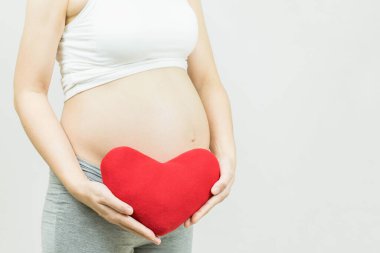 Gri arka planda kırmızı kalp taşıyan hamile kadın annelik, hamilelik, insanlar ve beklenti konsepti.
