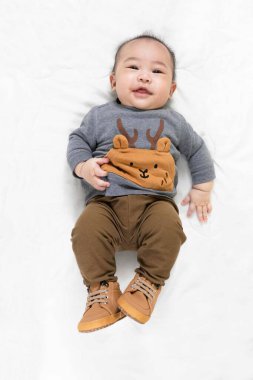 Hoş 4 ay, şık kıyafetler içinde küçük Asyalı erkek bebek ve yumuşak battaniyenin üzerine uzanmış bebek botları evde mutlu bir şekilde gülümsüyor.